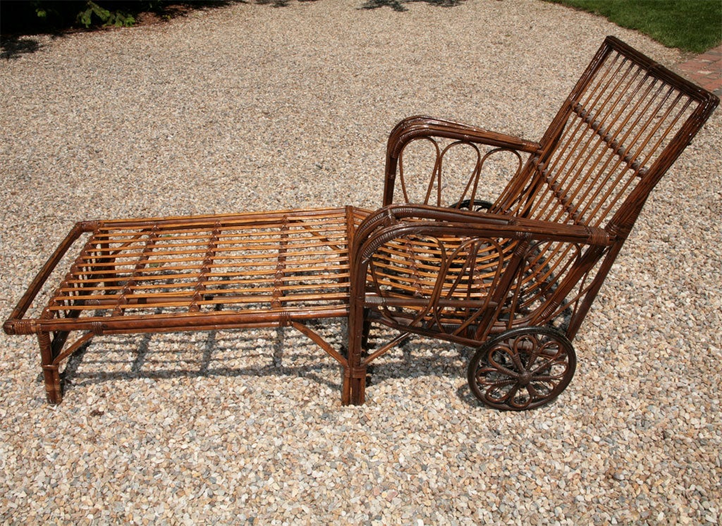 Unusual Stick Wicker chaise lounge with wheels for easy portability. Natural stained finish. Wide curved arms, magazine pocket woven into left arm, angled footrest with gallery. Decorative cane-wrapping on rattan looped wheels.