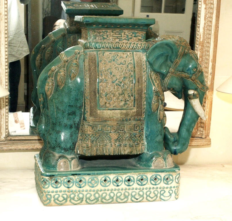 A CERAMIC ELEPHANT PREDOMINATELY TURQUOPISE WITH BRONZE COLORED DETAIL, SET UPON A CREAM AND TRUQUOISE FILIGREE RECTANGULAR BASE.