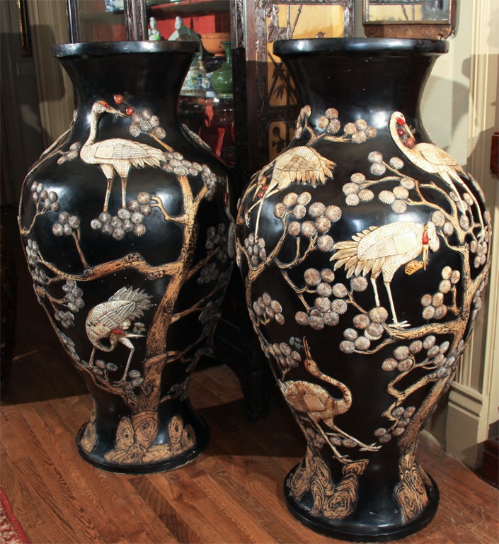 A very large pair of Japanese papier-mache lacquer urns with finely engraved exotic ivory cranes in deep relief carrying stems of colored soapstone cherries, entwined around scrolling carved cherry trees with blossoms of engraved ivory.  Chinoiserie