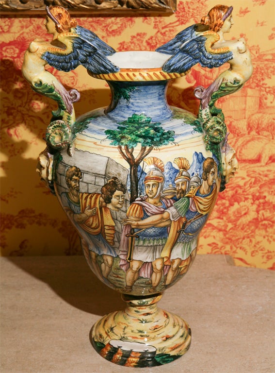 A PAIR OF HAND PAINTED MAJOLICA URNS, WITH ROMAN SCENES AND ANGEL HANDLES.