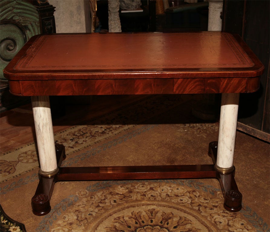 A very nice mahogany and crotch mahogany veneered writing table raised up on marble columns with bronze bases. The writing surface is leather with gold tooling. This table though not a period antique it is of great design and scale and the use of