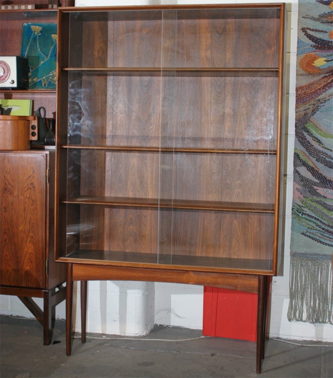 An elegant narrow rosewood vitrine with sliding glass doors.  Features vintage danish modern design, height adjustable shelves, beautiful wood grain, tapered legs, a detailed skirt and beveled edge.  Perfect for entryways and other narrow spaces.