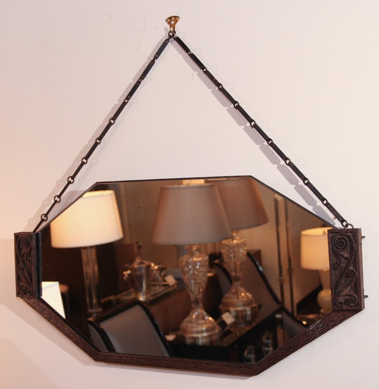 This gorgeous Art Deco mirror was realized in France, circa 1930. It features an octagonally shaped design housed in a patined bronze frame inscribed with Arts & Crafts floral details throughout, and a horse bit style chain. With its clean modernist