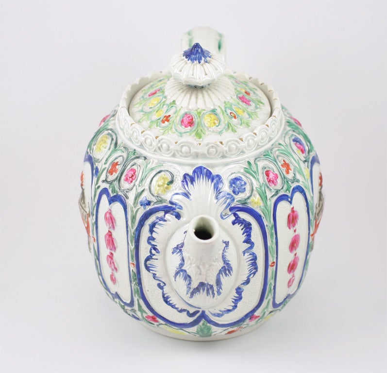 An English pearlware teapot molded with flowers and a classical urn and decorated in enamel colors