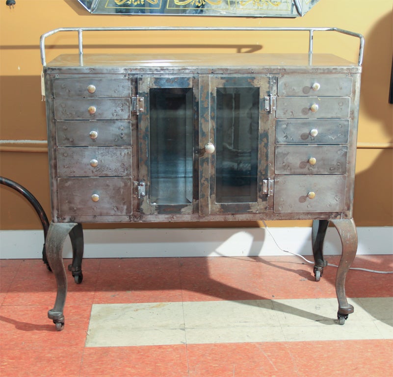 Early 20th century stripped steel dental/metal cabinet on casters;  very clean with great patina and stylized cabriole legs; beveled glass doors in the center flanked with five drawers at each side.