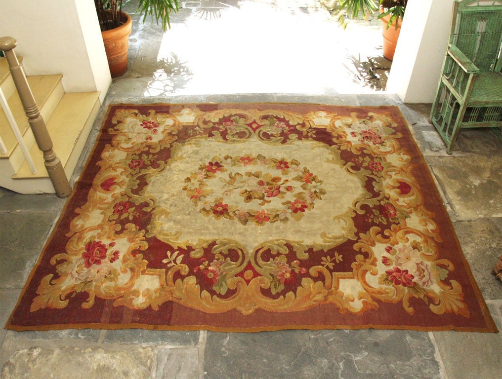 This Aubusson rug is from the Napoleon III era, with center floral medallion on beige ground, surrounded with floral garlands and cartouches on dark red ground.