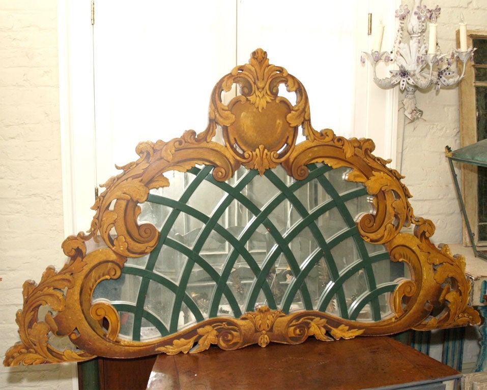 A  pediment or fronton, originally designed as an architectural ornament. It is painted and gilded with a trompe l'oeil cartouche and treillage backed with a mirror. For use perhaps as a headboard.