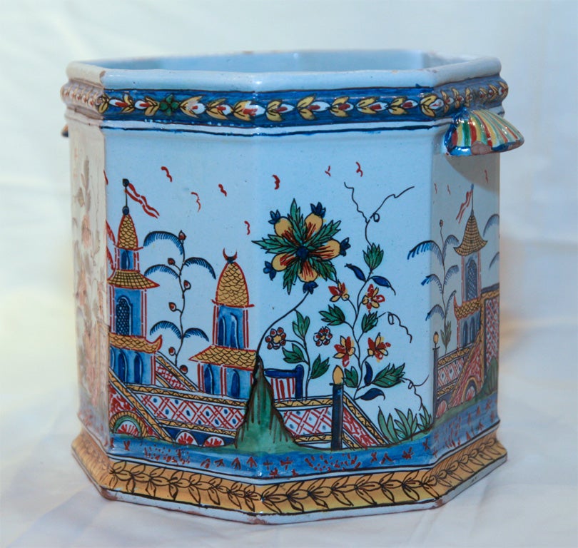 A pair of Rouen, French faience, octagonal cache pots painted in a traditional cashmere palette showing a scene of gardens with flowers and garden walls with castle towers