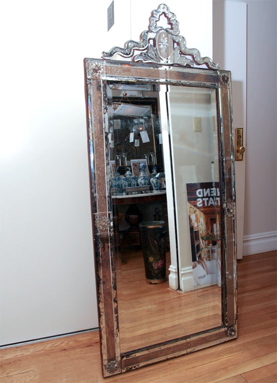 A French mirror with unusual reverse glass decorated frame, having bands of gold/copper leaf behind smoky mirrored glass secured by rosettes. The top surmounted by a trompe l'oeil mirrored ribbon.