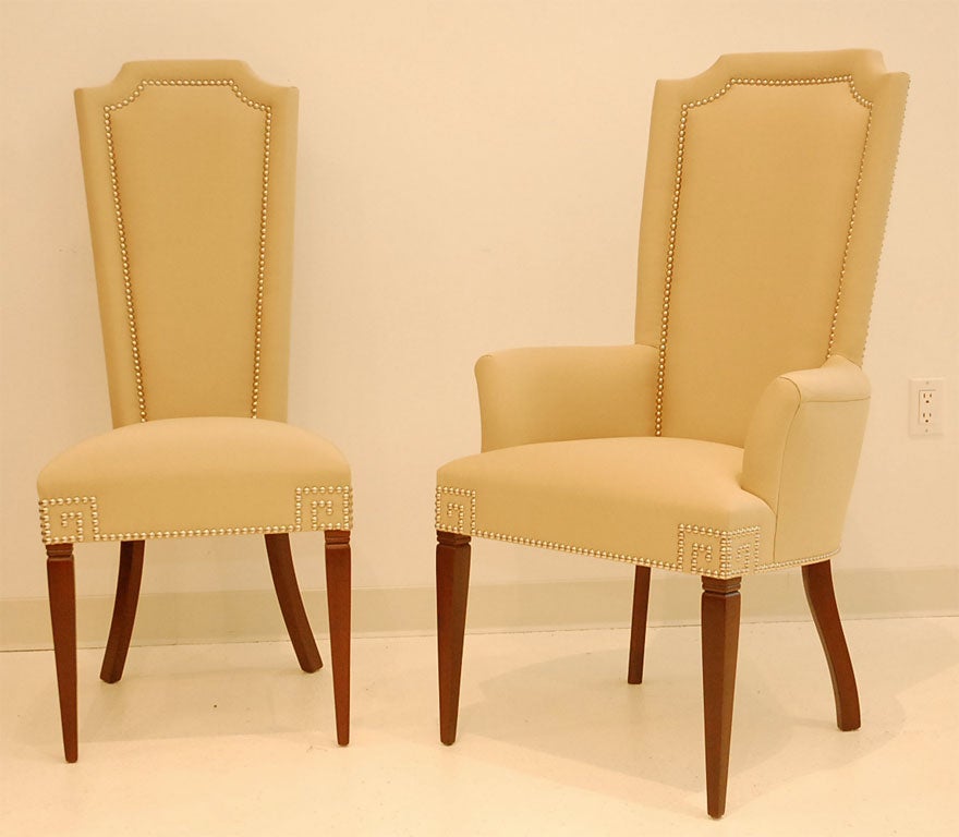 This unique set of dining chairs, consisting of twelve side chairs and two arm chairs, has been recently reupholstered in a glamorous polished cotton/silk blend- shot through with gold lurex- and finished with nickel head Greek key detail.  The