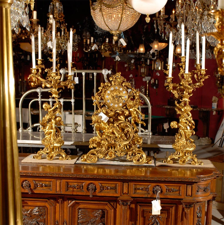 Very fine gilt bronze Rococo style garniture set depicting frolicking cherubs and a satyr. The clock is 31 inches high and 24 inches wide. The candelabra are 36 inches tall.