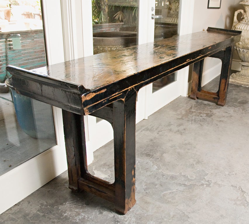 A one of a kind altar table, traces of wood visible through the original black lacquer, solid 2 ½” thick plank top with an additional 1 1/2” thick apron, wings, rectangular shaped legs with flared feet, stretchers with inset carved panels above,