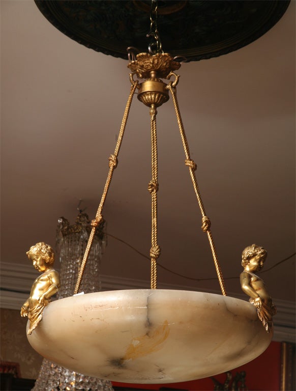 Gilt bronze and alabaster chandelier, the circular shade surmounted with three gilt bronze Putti suspended by three gilt bronze twisted ropes from a gilt bronze urn shaped ceiling plate.
