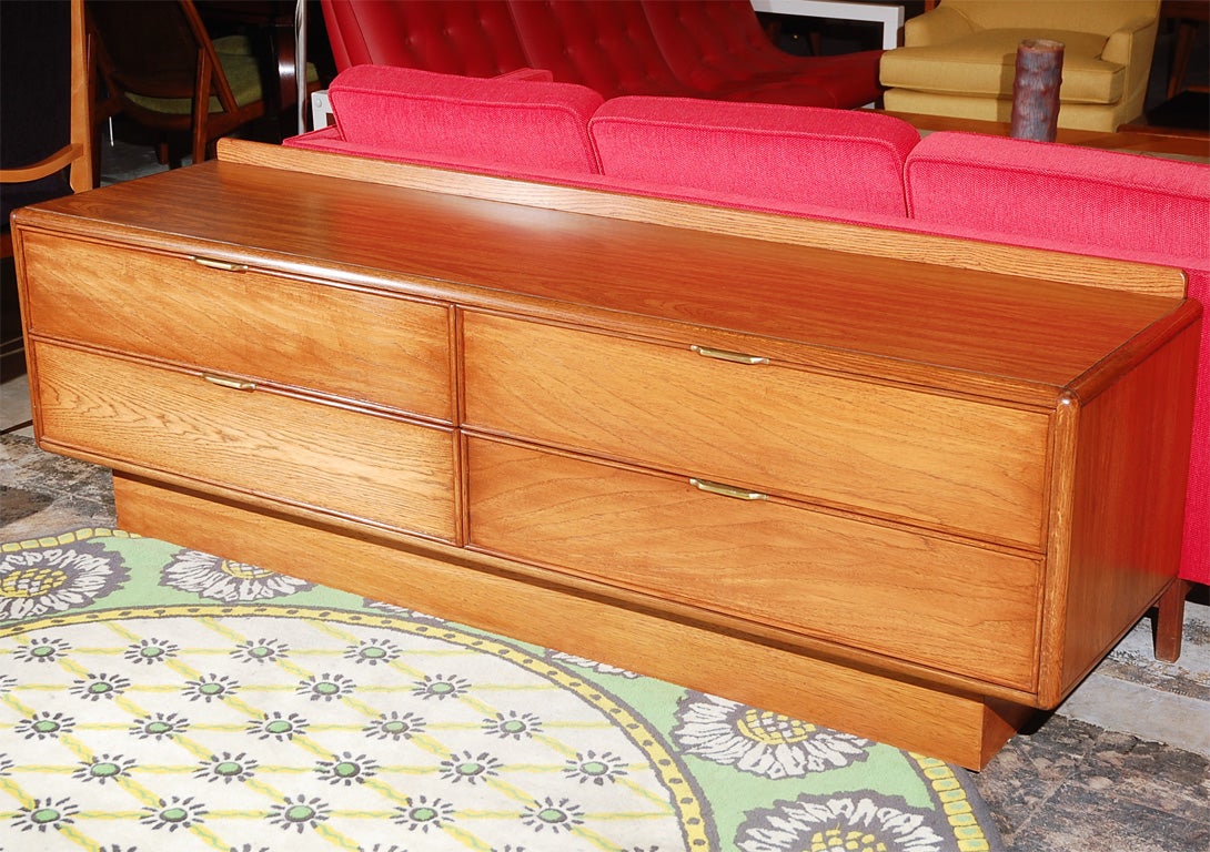 A long low dresser/credenza on a plinth base, with four drawers, thin brass pulls and raised back edge to keep objects from rolling behind the unit.