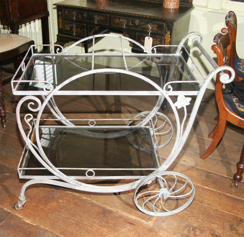 A two-tiered original patinated finish wrought iron & smoked-glass drinks<br />
or tea cart; on two wheels and two casters.