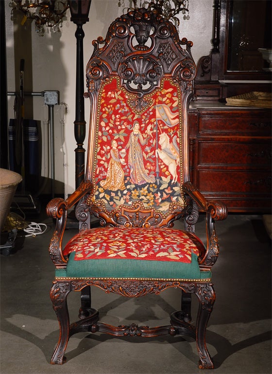 Chair fit for a king! This is a BIG French heavily carved C. 1900 walnut throne chair upholstered in needle and petit point. The carving is very intricate with leaves, shells, baskets, etc, and it's beautifully upholstered in a needle/petit point.
