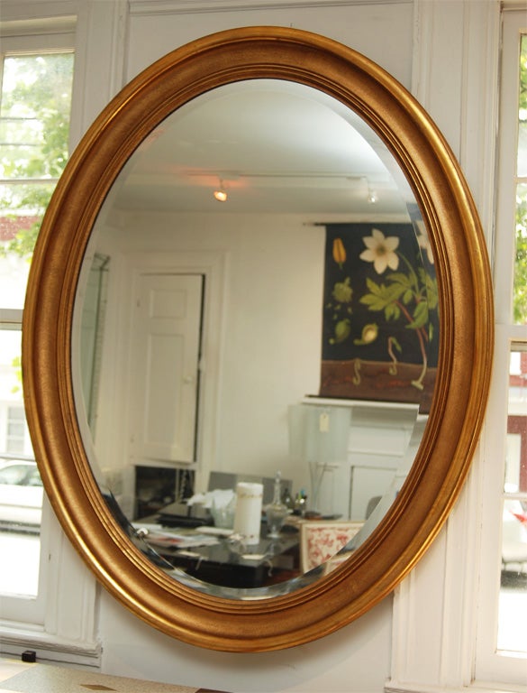 Hand carved wooden gold leafed oval frame with beveled contemporary mirror, substantional heft and beautiful burnished patina