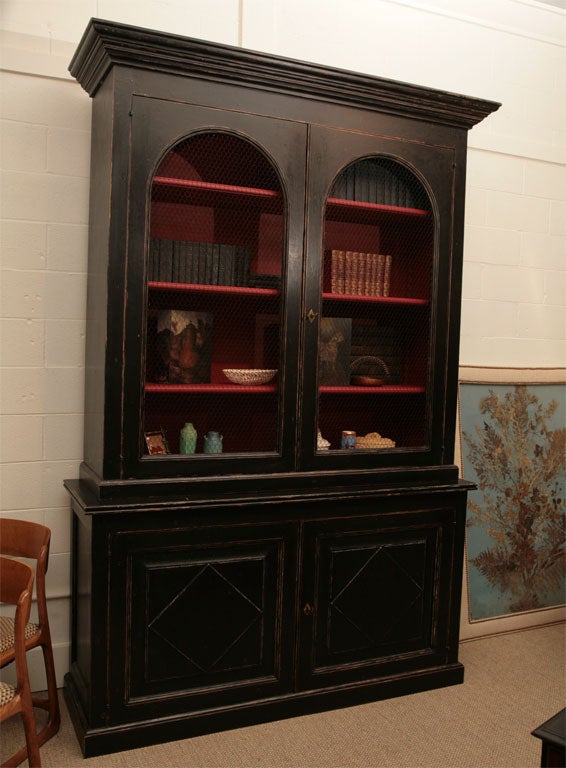 Here is a Regency style painted black cabinet with a red interior. This large scaled cabinet features brass chicken wire screen doors and adjustable shelves.