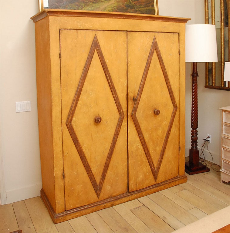 The armoire cabinet in pinewood is accented with a molded cornice over a body with raised diamond design on the doors with round knobs and raised on a low plinth base.
