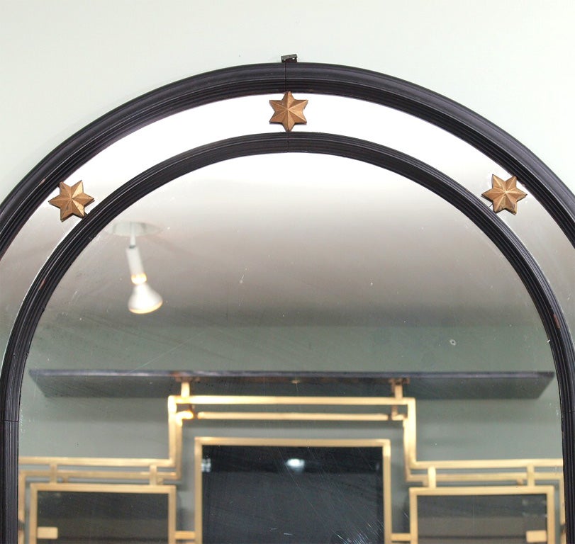 Arched mirror with frame in ebonized wood accented with gilt six-point wooden stars at the edges and center; shaped bottom rail