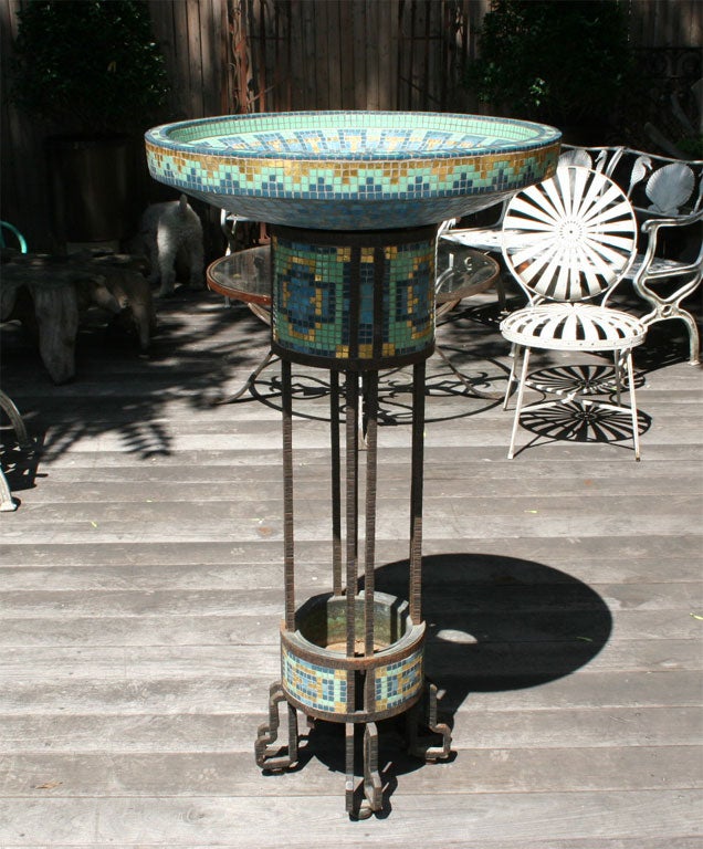 A French forged iron fountain with gold and polychrome detailed bowl having clear glass bottom illuminated by electric sockets supported by forged iron stand. Marked by makers Cabel.