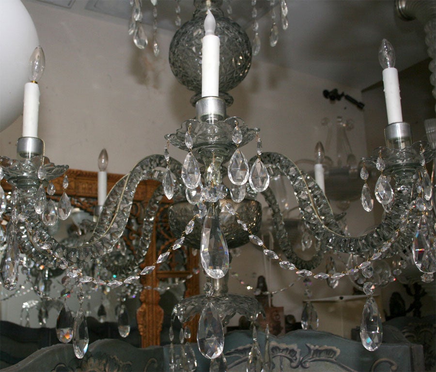 An English 8-light George III period candle powered chandelier, now electrified*, with hand cut S-shaped crystal arms issuing from star patterned cut crystal bowl above vase and umbrella shaped elements with faceted crystal ball on underside. Each