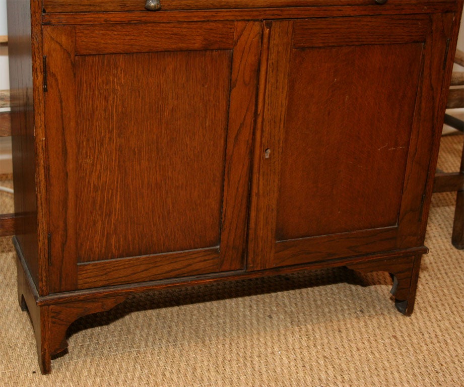 Early 20th Century Arts and Crafts Style Drop Front Oak Desk,  the drop front opening to pigeon holes above a single drawer with ribbon tie pulls and a double door closed bookshelf. The desk top 20 1/2 inches deep when open.<br />
<br />
To see