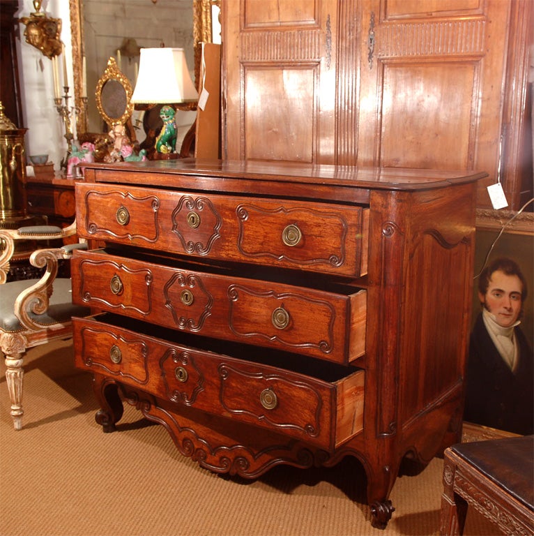 a Louis XV French provincial walnut chest, three drawers with a large apron at base, curving decoration carved on drawers at sides, around key hole and on apron, round brasses and escutcheons