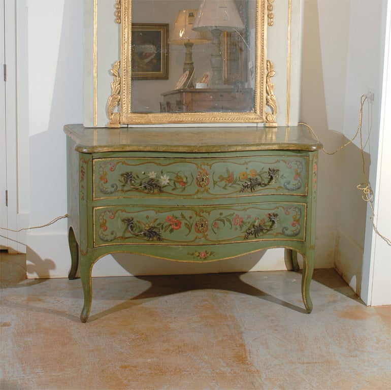 An Italian Rococo style green painted two-drawer commode from the 19th century. This exquisite Italian chest of drawers is painted in a soft green color with gilded highlights. Delicate painted cartouches on the drawers surround floral motifs with