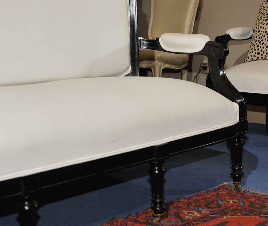 The arched crestrail continuing to volute scrolled padded arms over a fitted back and seat raised on tapered reeded legs on casters.  Upholstered in white cotton duck with black & white toile on reverse.