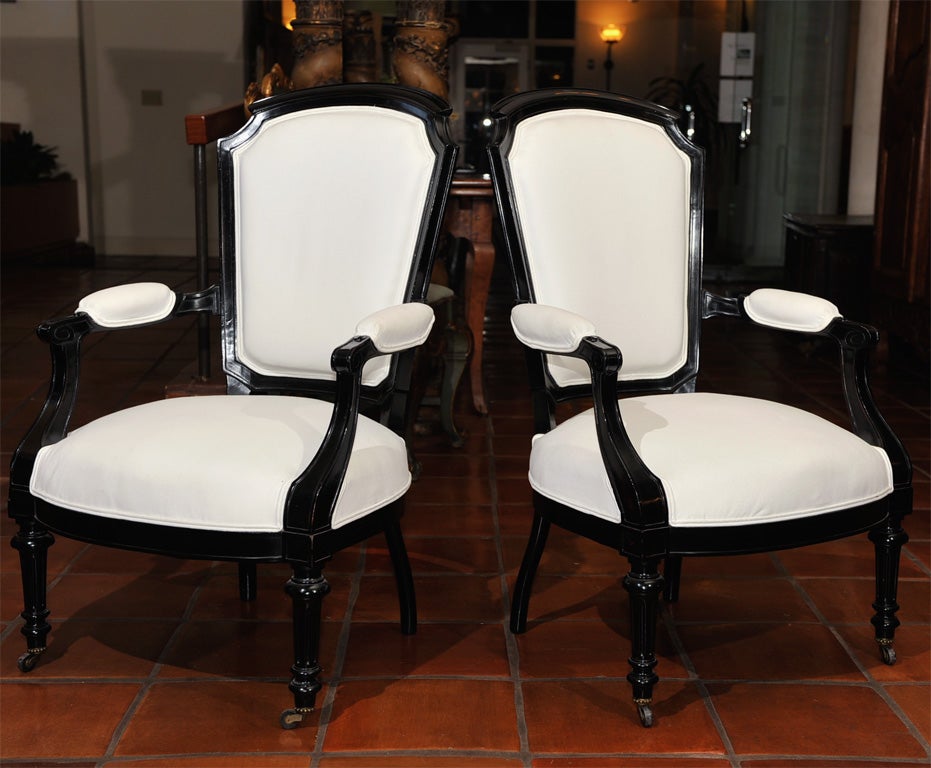 Each with arched crestrail continuing to volute scrolled padded arms over a fitted back and seat raised on tapered reeded legs on casters.  Upholstered in whit cotton duck with black & white toile on reverse.