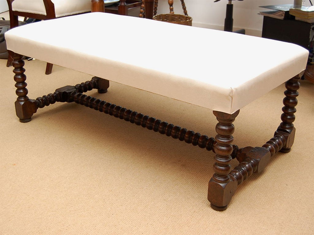 An upholstered coffee table made in England with bobbin legs and upholstered in white muslin. Can also be used as a seating hassock.