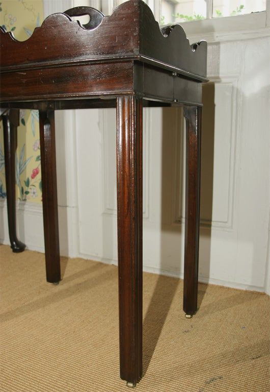 George III mahogany bottle carrier with six compartments and pierced shaped handle on a concertina folding stand with fluted chamfered legs on leather castors, the hinges stamped 