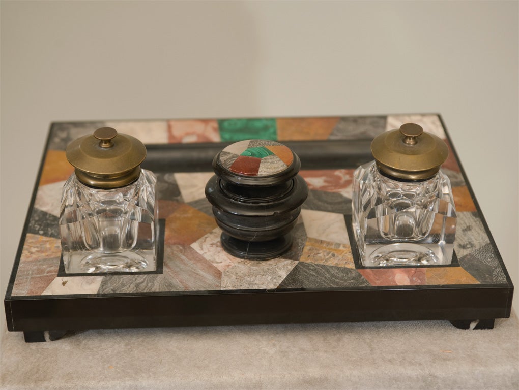 A late 19th century Italian Pietra Dura inkstand; with two removable blown glass inkwells with brass tops flanking a central marble inkwell all raised on curved marble feet.