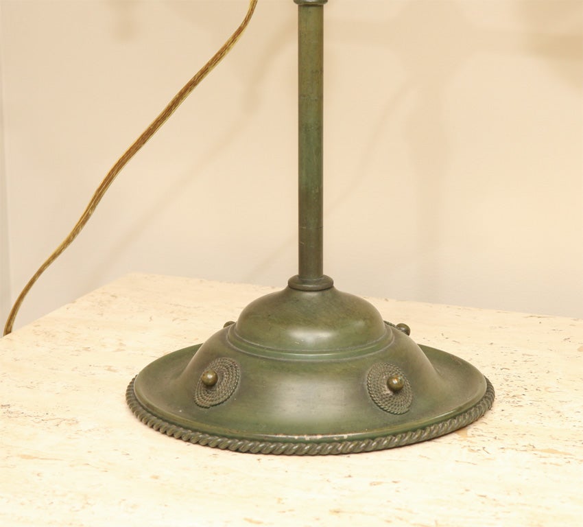 An American Arts& Crafts Tiffany style single arm student lamp with applied braided edges on oil ressets and base having applied rosettes. The top with amber colored half dome shade.
