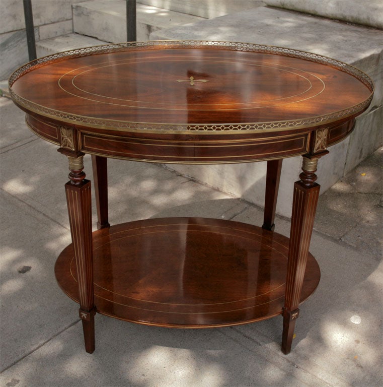 This very nice brass galleried mahogany oval table is further decorated with corresponding brass bands and a modified brass compass point to the top. The choice of woods is exceptional and dramatically figured.The legs and lower shelf are also