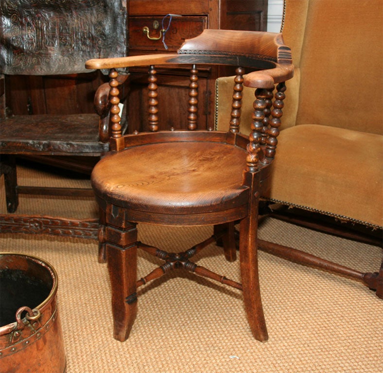 An English 19th C corner chair with curved back rest and arm supports on bobbin turned back spindles over round seat on curved tapered legs joined by turned stretcher. A very sculptural and unique form.