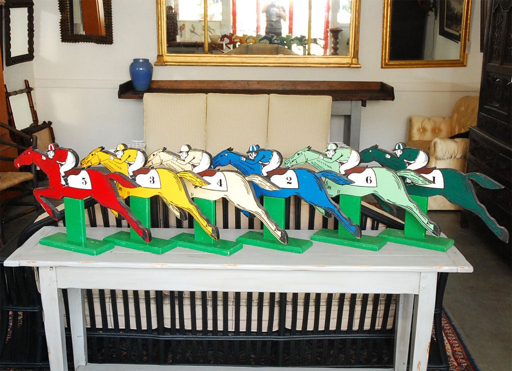 A set of six horse racing figures with mounted riders dating from the first half of the 20th century. The figures are painted in individual colors with black and white hi-lights. All figures stand on green painted pedestals. There is a long canvas 
