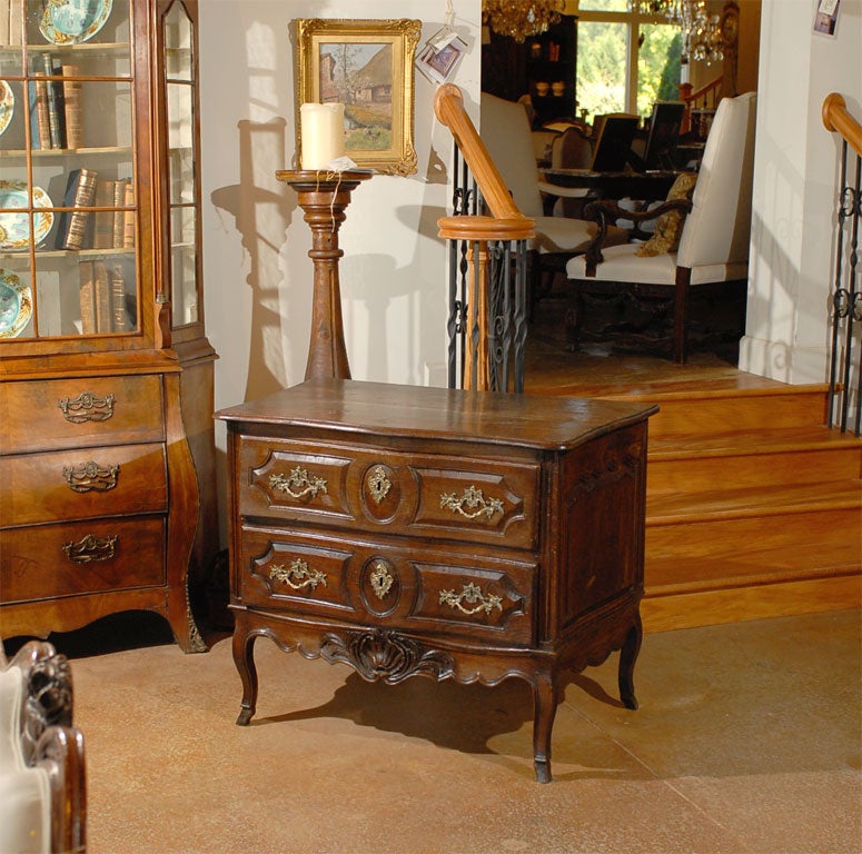 A French Louis XV period petite walnut two-drawer commode with carved apron from the mid-18th century. This charming French commode features a serpentine top sitting above two drawers. Each drawer is decorated with carved panels framing the Rococo