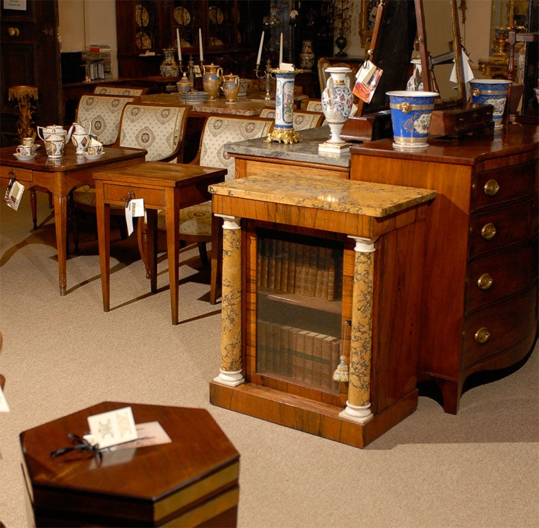 A Regency rosewood side cabinet with glass inset door within a larger hidden door, scagliola top and column uprights, and adjustable shelving.  This piece originated in England during the first quarter of the 19th century.

William Word Fine