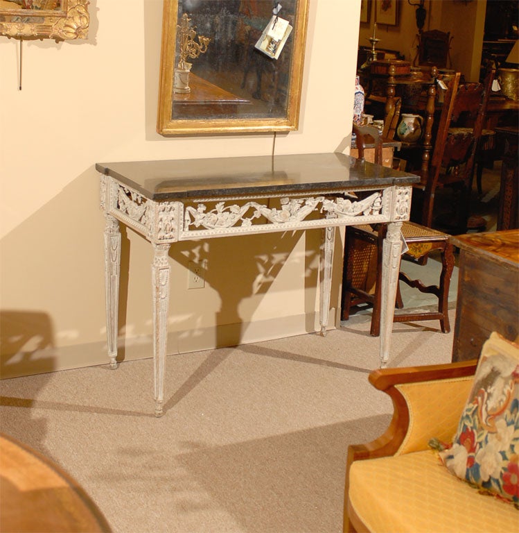 A Louis XVI Period white painted console table with carved pierced frieze and rectangular black marble top, originating in France during the late 1700s.

The rectangular marble top rests atop a pierced frieze, carved with fruits suspended in