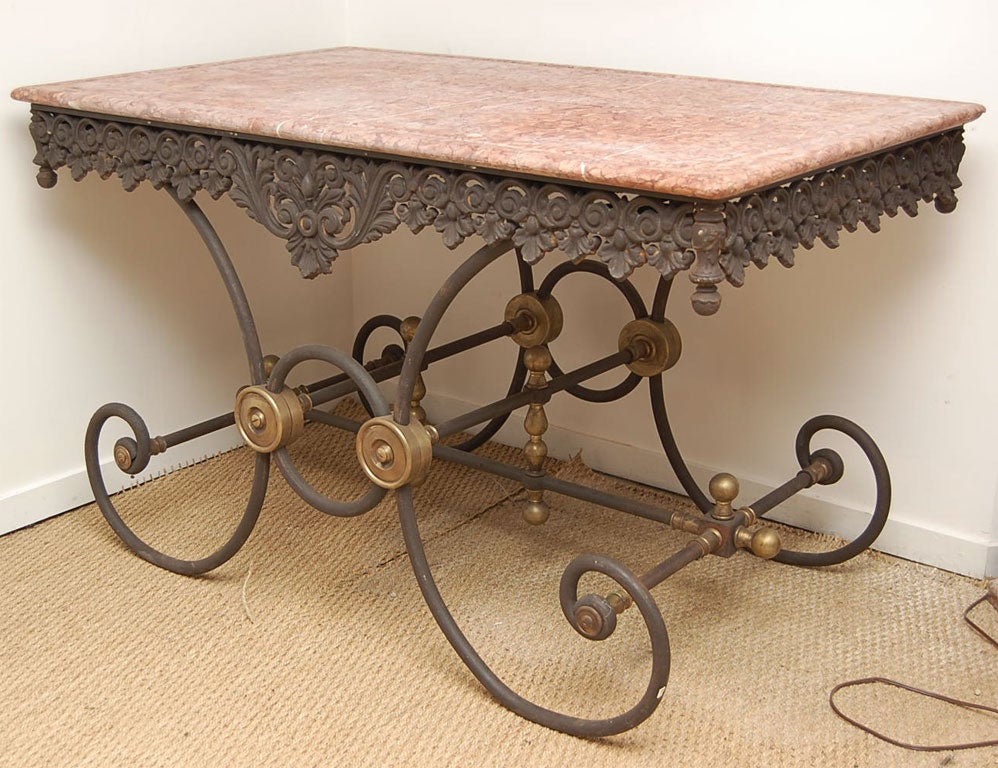 A cast iron bakers table with scroll legs, highly decorative apron, attractive brass accents and a beautifully veined rose marble top.