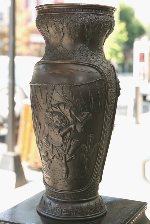 Ce grand et impressionnant vase en bronze coulé est d'un type appelé bronze de Tokyo. Elle présente des éléments de l'iconographie japonaise et chinoise et est non seulement moulée à la cire perdue, mais elle est ensuite travaillée avec des têtes de