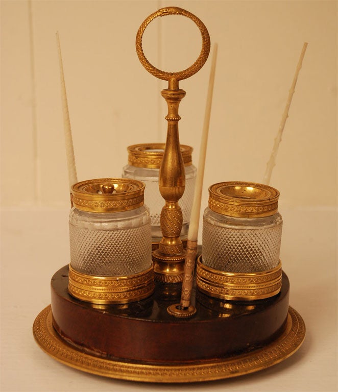 Of circular form with round cast and chased serpent handle on a baluster stem and circular base mounted with paired turned rings enclosing three cylindrical cut glass containers alternating pen holders on a berried laurel ring cast plinth, with ball