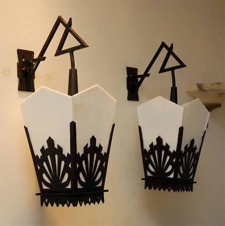 Pair of Asian-style black iron lanterns with milk glass panels. Decorative wrought iron wall-mounts with triangular details suspend charming asian inspired angular lanterns.