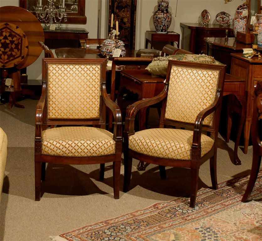 A pair of Empire Period French carved mahogany fauteuils from the early 19th century.

Each with a rectangular padded back with downcurved reeded arms, the bow front upholstered seat on sabre legs headed by stylized lotus leaves.
