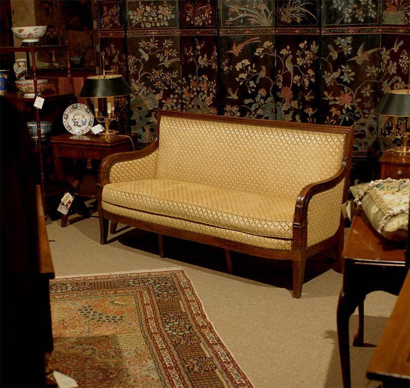 An Empire Period French mahogany settee with rectangular padded back with downcurved reeded arms, the bowfront upholstered seat on sabre legs headed by stylized lotus leaves.  Originating in France during the first quarter of the 19th century.
