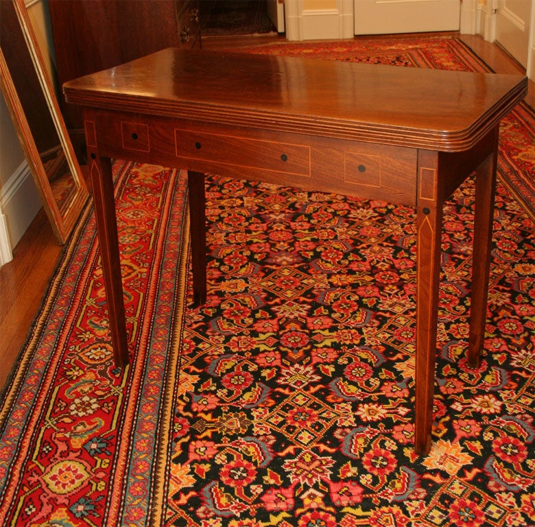 A beautiful mahogany card table with reeded top, inlay and ebonized detail on apron, raised on square legs.  The top is hinged and opens up over gate leg.