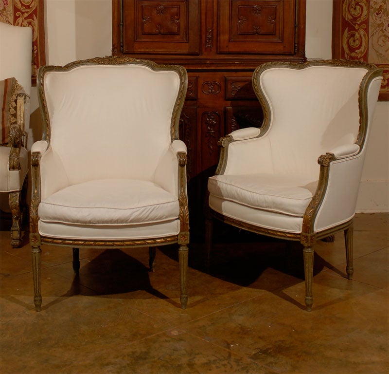 A pair of French Louis XVI style wingback bergères chairs from the 19th century, with green and gold tones and new upholstery. Born in France during the 19th century, each of this pair of bergères-à-oreilles features a wingback, carved with foliage