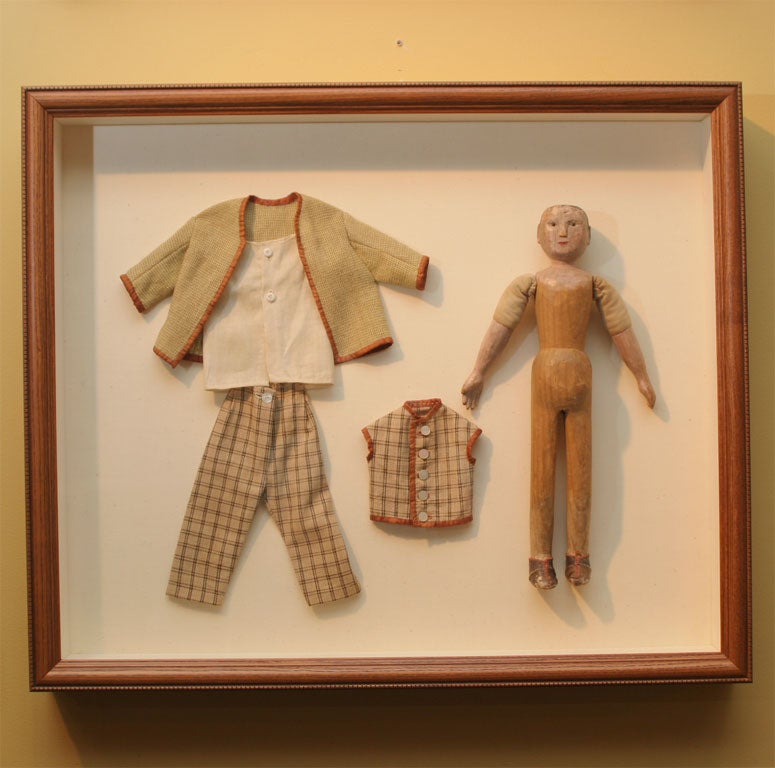 Folky carved wooden boy doll with original painted surface and leather shoes. Clothes original to doll. Archivally framed behind ultraviolent plexiglass in wood shadowbox with beaded edge.